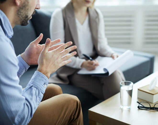 Patient of counselor explaining his trouble while sitting by table in front of psychologist during session