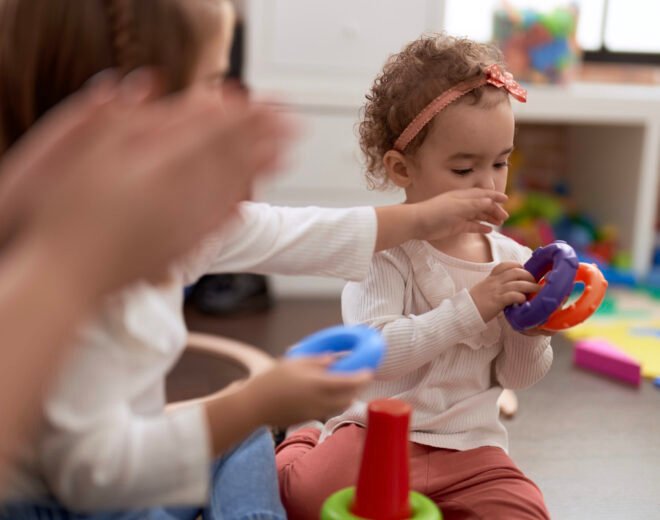Adorable caucasian girl playing with hoops sitting on floor at kindergarten