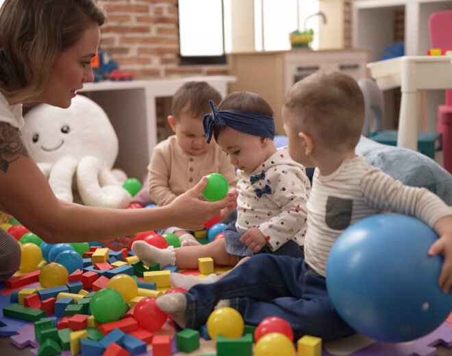 Teacher and preschool students playing with balls sitting on floor at kindergarten